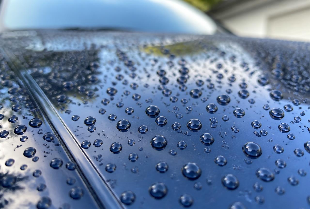 Tight water beads standing on the glossy dark blue paint of a coated car after rinsing